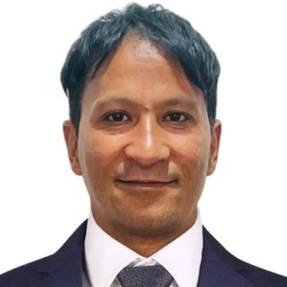 A man with short, dark hair wearing a suit and tie smiles slightly against a white background, conveying professionalism and warmth.