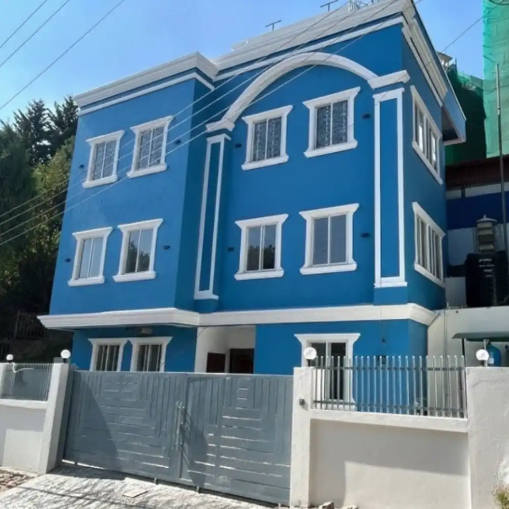 A vibrant blue, three-story building with white trim and large windows. The metal gate and fence add a modern touch. The mood is welcoming and lively.