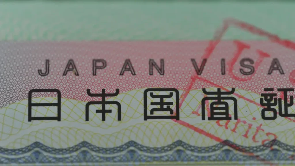 Close-up of a Japan visa with "JAPAN VISA" printed in black on a red and green gradient background, featuring intricate patterns and Japanese characters.